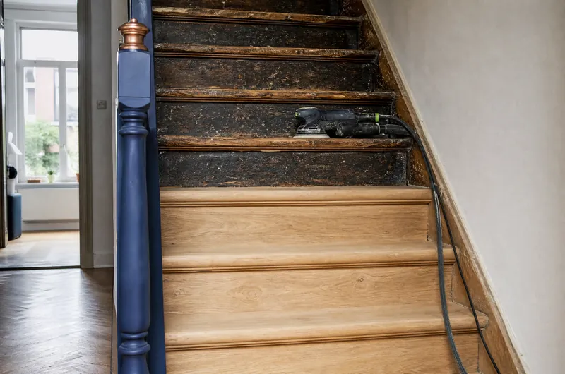 Escalier en bois en cours de rénovation : marches poncées et vitrifiées en bas, anciennes en haut